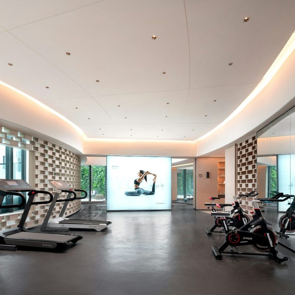 Gimnasio moderno con cintas de correr y una pantalla grande. Decoración minimalista.